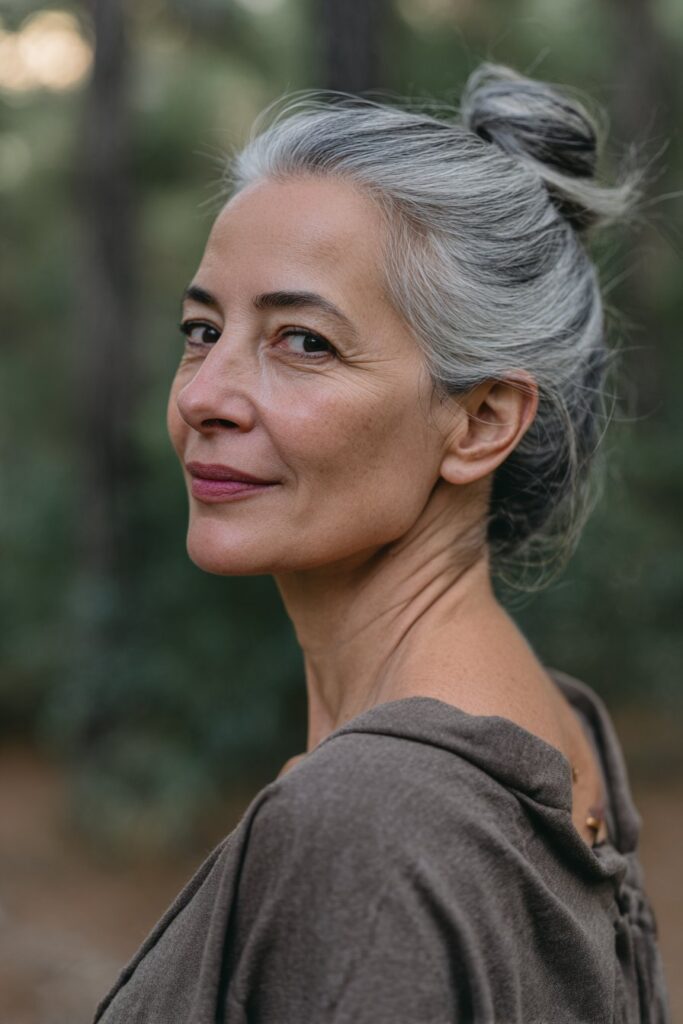 Retro 90s inspired bun for women over 60, with salt-and-pepper tones, set against a natural forest scene.