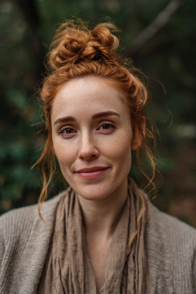 Adorable bow-tie bun for women over 60, with strawberry blonde glow, set against a natural forest scene.