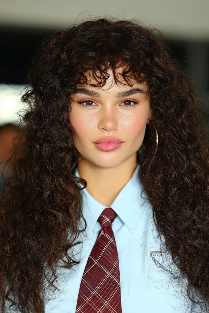 School girl with soft curly curtain bangs, framing her face naturally for a pretty school day look.