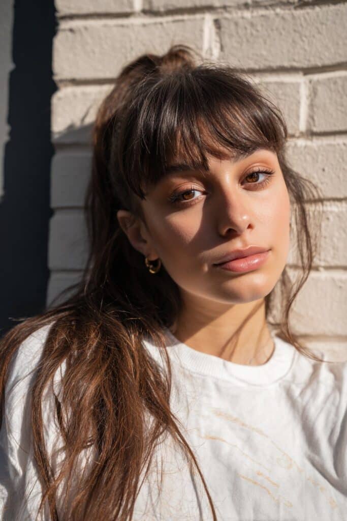 Tousled ponytail styled with curtain bangs that softly frame the face.