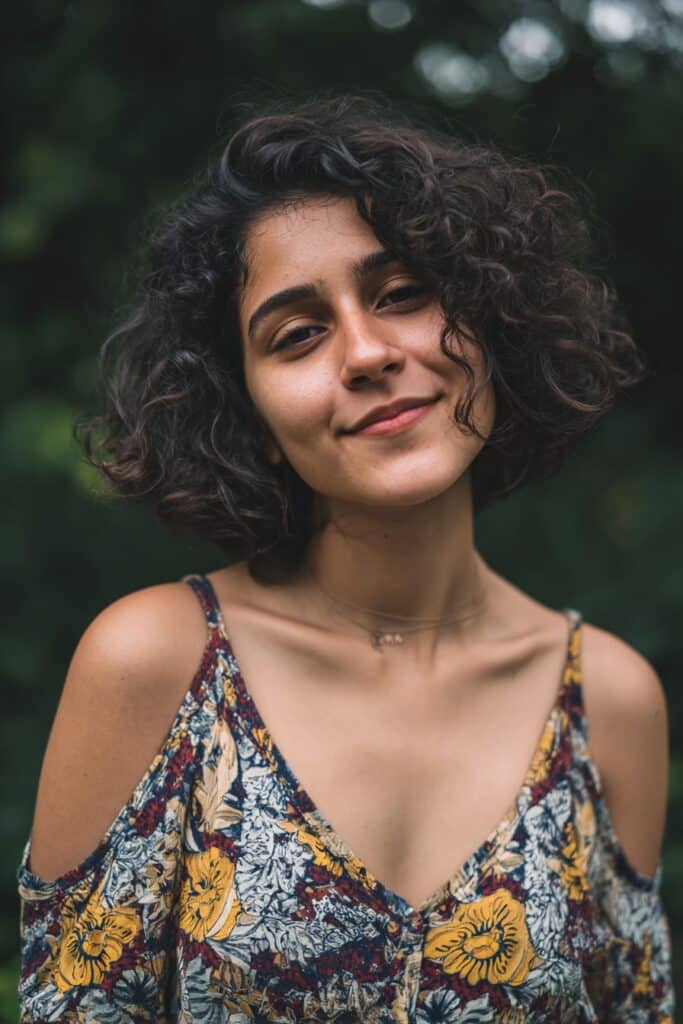 Curls gathered high on top of the head in a loose pineapple style to preserve volume and shape.